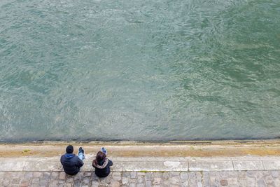 Directly above shot of man and woman sitting on retaining wall in front of river