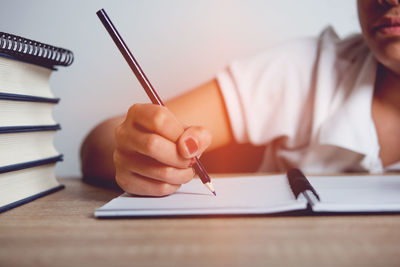 Midsection of woman writing in book on table