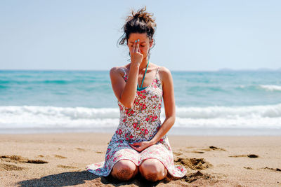 Woman praying while sitting at beach against sky