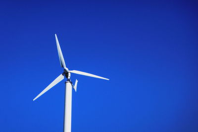 Low angle view of wind turbine against clear blue sky