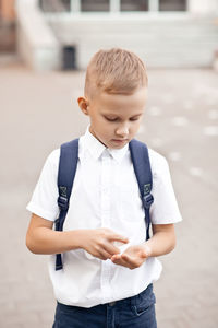 Schoolboy using hand sanitizer outdoors