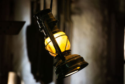 Close-up of illuminated electric lamp hanging against wall