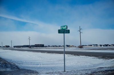 Country road passing through snow covered land against sky