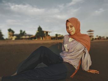 Portrait of young woman sitting against sky