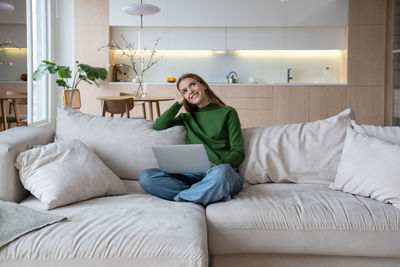 Woman freelancer sitting on couch at home working on laptop creating new ideas for working project.