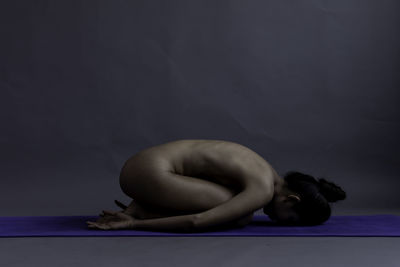 Full length of naked woman sitting against gray background