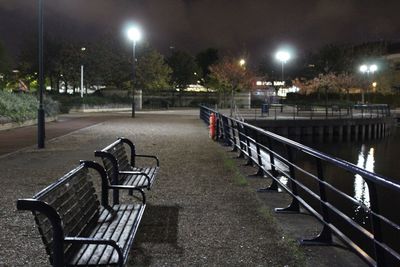 Empty bench by street at night