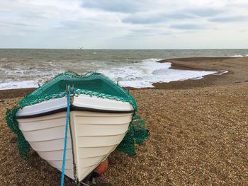 Boat moored at beach against cloudy sky