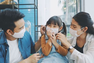 Close-up of smiling family wearing flu mask sitting at home