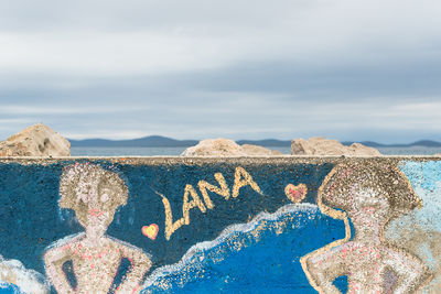 Close-up of graffiti on retaining wall against sky