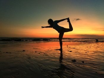 Silhouette woman doing yoga on beach against sky during sunset