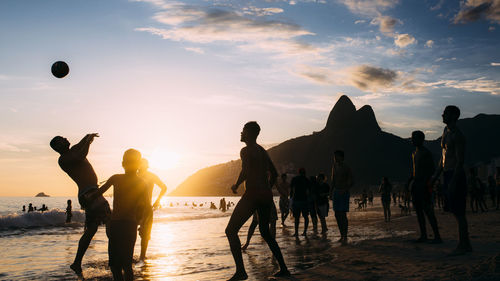 People at beach against sky during sunset