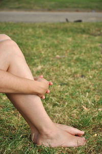 Low section of woman hugging knees on field