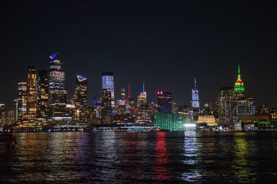 Illuminated buildings by river against sky in city at night