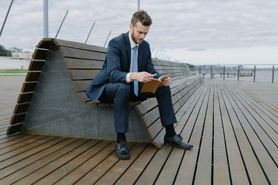 Young businessman reading book while sitting on bench