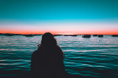 Silhouette woman sitting at beach against sky during sunset