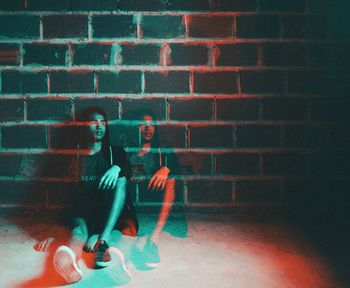 Double exposure of man sitting against wall