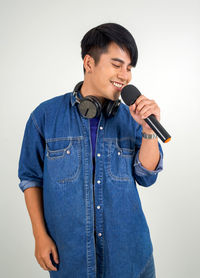 Smiling man holding camera while standing against white background