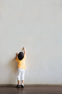 Rear view of boy standing against wall at home