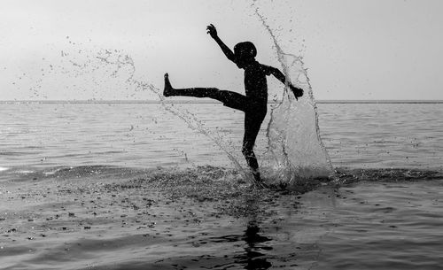 Boy splashing water in sea against sky