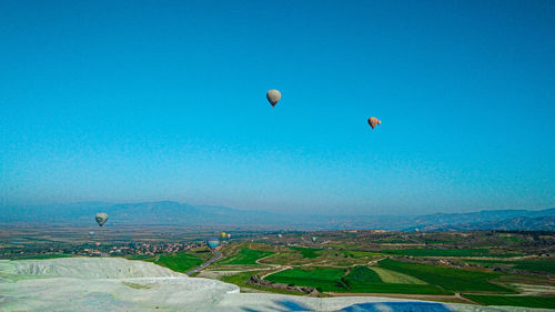 Hot air balloons flying over landscape against blue sky