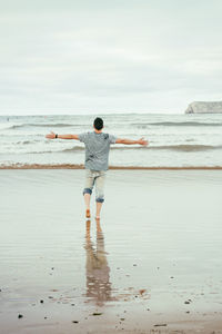 Rear view of woman standing on beach against sky