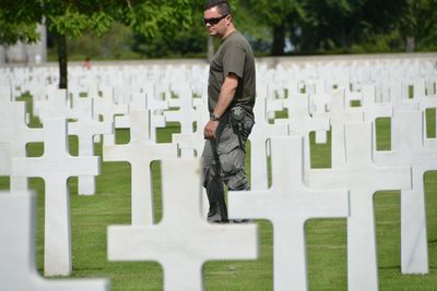 Side view of mature man wearing sunglasses standing amidst cross in cemetery