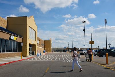 Woman walking on city street against sky