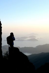 Silhouette male hiker photographing sea against sky