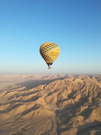 Hot air balloon flying over desert against clear blue sky