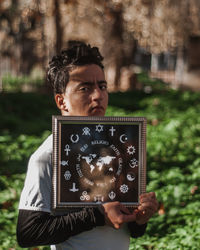 Portrait of man holding frame while standing outdoors