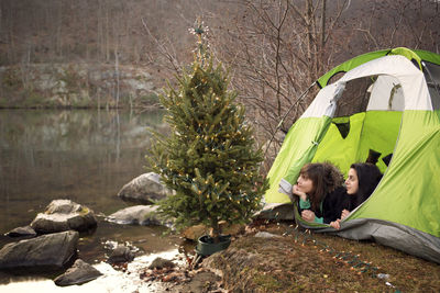 Friends looking away while lying in tent by christmas tree