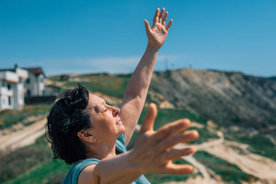 Side view of man with arms raised against sky