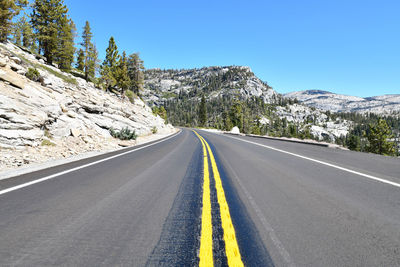 Road amidst trees and mountains against clear sky