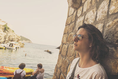 Thoughtful woman standing by wall against sea