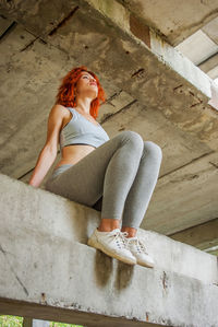 Low angle view of redhead woman sitting on retaining wall