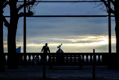 Silhouette people on railing by sea against sky during sunset