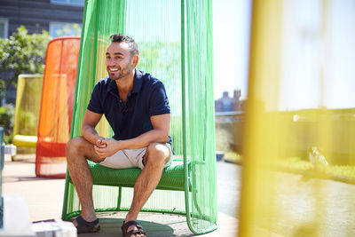 A man sits in a colorful chair on a modern patio.