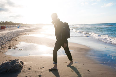 Full length of man walking at beach against sky on sunny day