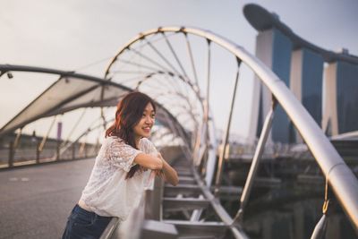 Young woman on bridge in city against sky