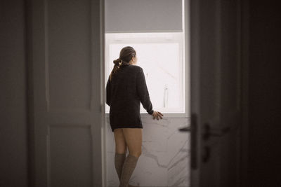 Rear view of woman standing against window