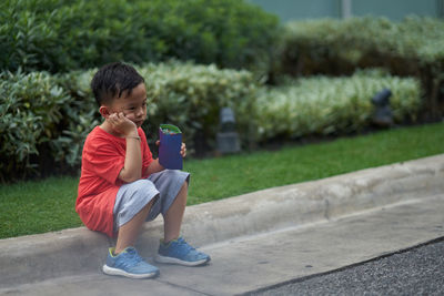 Thoughtful boy with container sitting on footpath