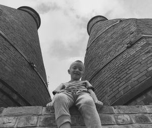 Low angle portrait of happy boy sitting amidst tower against sky