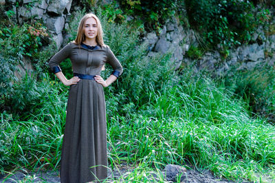 Portrait of young woman in dress standing against rock formation