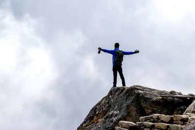 Low angle view of man standing on rock against sky