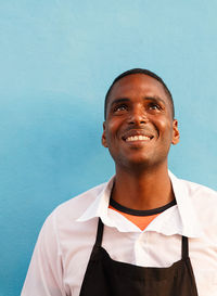 Smiling young man looking away against blue wall