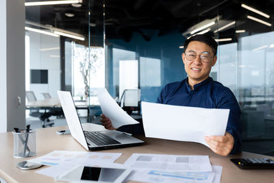 Portrait of young man using laptop while standing in office