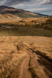 Dirt road amidst landscape against sky