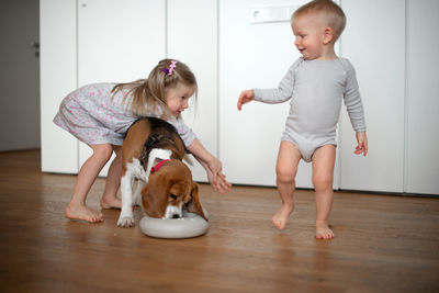 Full length of girl and baby boy playing with dog at home