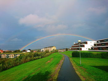 Rainbow over road by buildings in city against sky